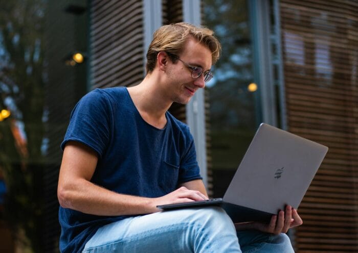 A young man sitting outdoors in Leiden, Netherlands, working on a laptop.