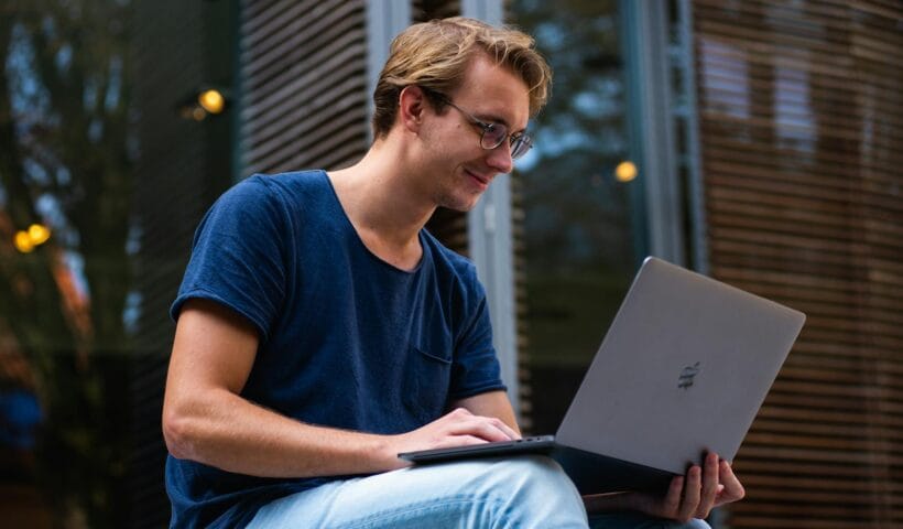A young man sitting outdoors in Leiden, Netherlands, working on a laptop.